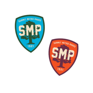 A group of two shields, one orange and one blue, with a border and tree in the background. Across the front of the tree in bold letters is SMP.