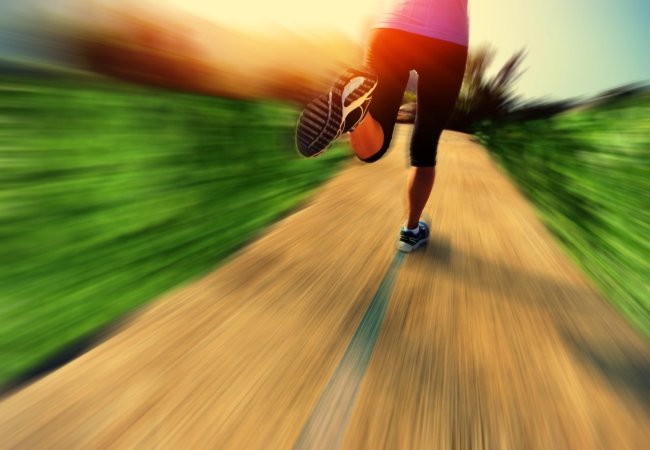 The bottom half of a person is seen running along a trail.