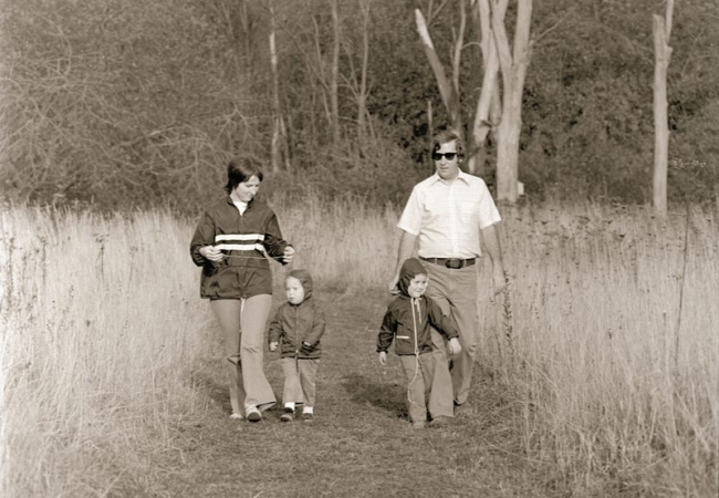 A black and white photo of a couple and two children hiking through a meadow.
