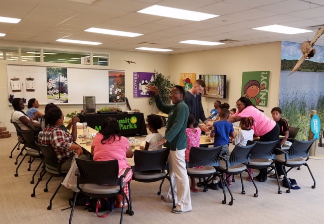 A group of kids and young adults sit around a u-shaped table inside the pop-up nature center at Summit Lake.
