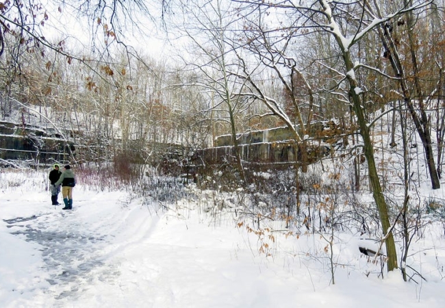 Snow covers Deep Lock Quarry and the surrounding landscape. Two people bundled in winter clothing stand in the distance.