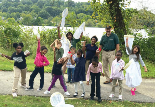 A group of children along with two Metro Parks naturalists hold of a variety of bug nets and bug jars while standing on the Towpath Trail.