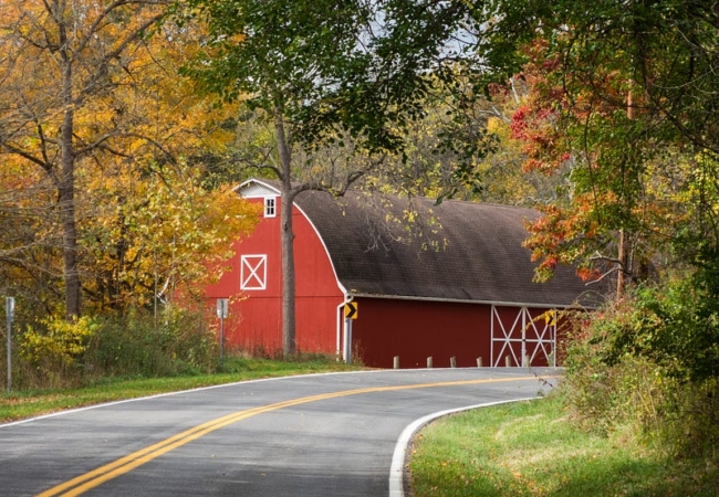A red barn sits along a curved road surrounded by trees.