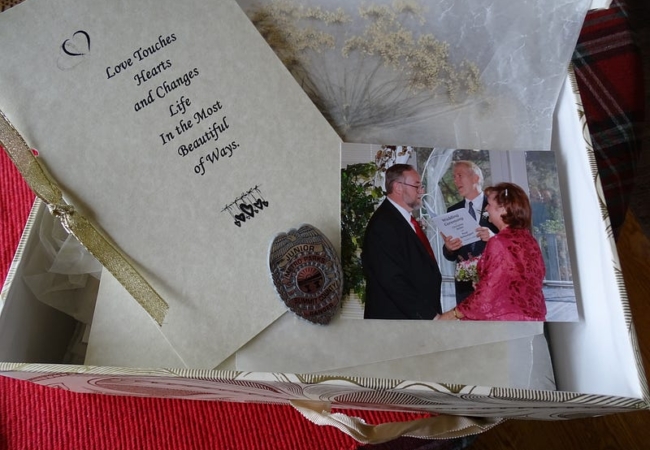 A box holds a pressed white flower, a photo of a wedding, a Junior Metro Parks ranger badge, and a decorative paper that reads, "Love touches hearts and changes life in the most beautiful of ways."