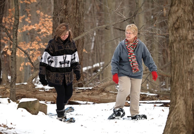 Two women snowshoeing on a snowy trail in the woods.