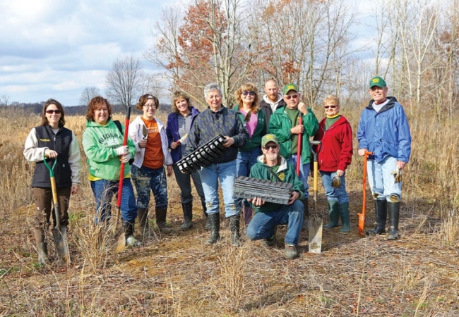 A group of volunteers pose with shovels and empty plant containers.