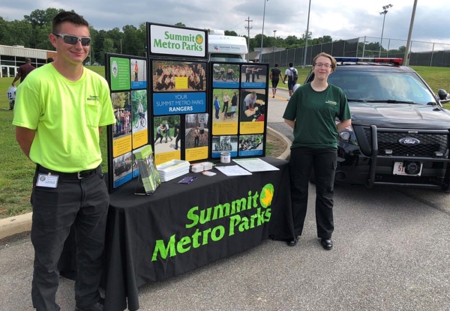 Two Ranger Explorers stand on either side of a table, which holds a display offering additional information about the program.
