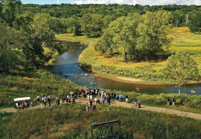 Kayakers float through the Cuyahoga River at the Valley View Area of Cascade Valley Metro Park while several people watch from shore.