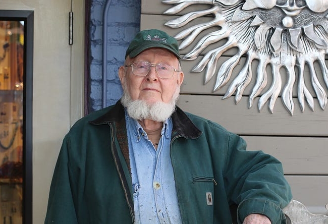 A portrait of Don Drumm. He is standing in front of one of his iconic sun art pieces.