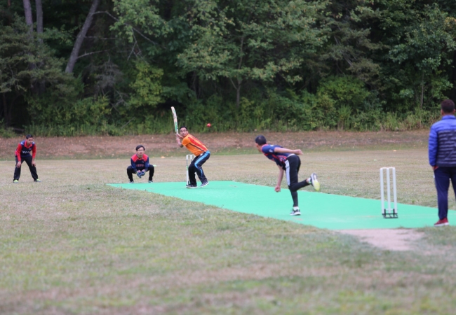 A group of people play cricket in a field.