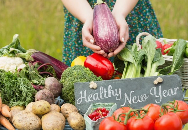 A table of fresh produce, including potatoes, beets, broccoli and tomatoes, with a sign in the middle that reads, "Healthy New Year."