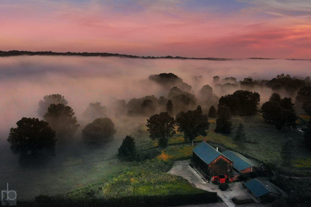 Aerial view of the old clubhouse and surrounding trees on a foggy sunrise with pink and blue skies
