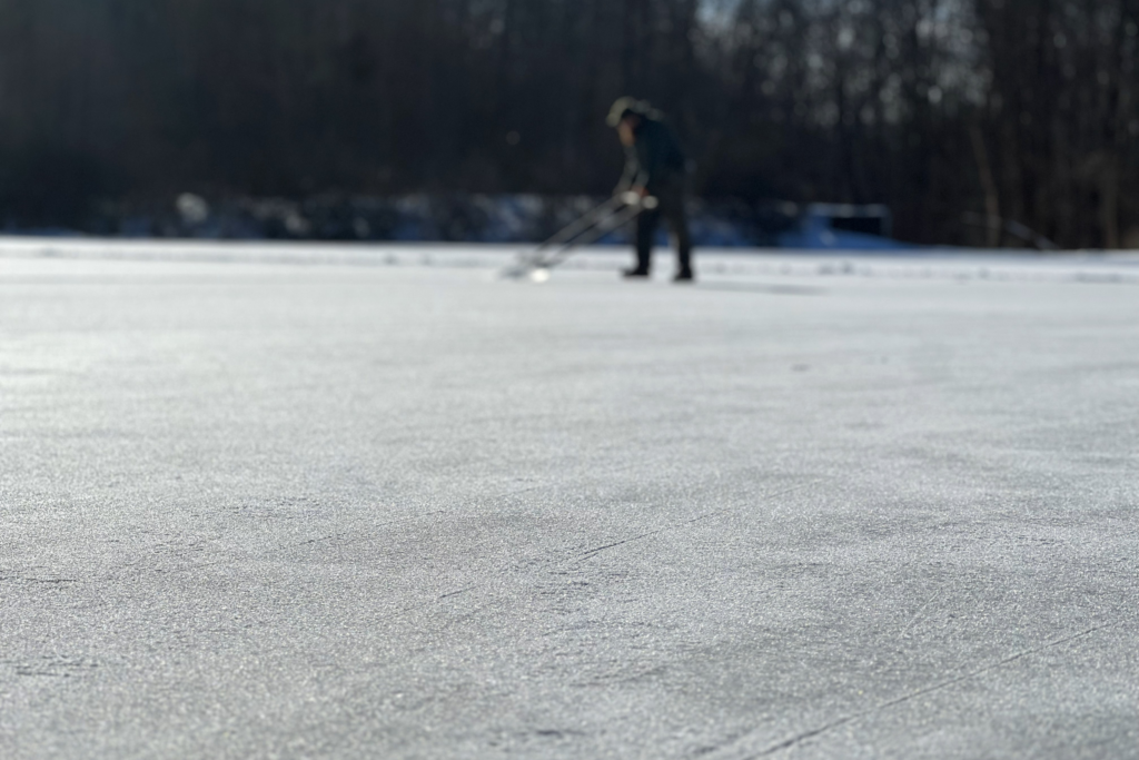 prepared ice on Brushwood Lake is in focus in the foreground while a figure clears snow in the background