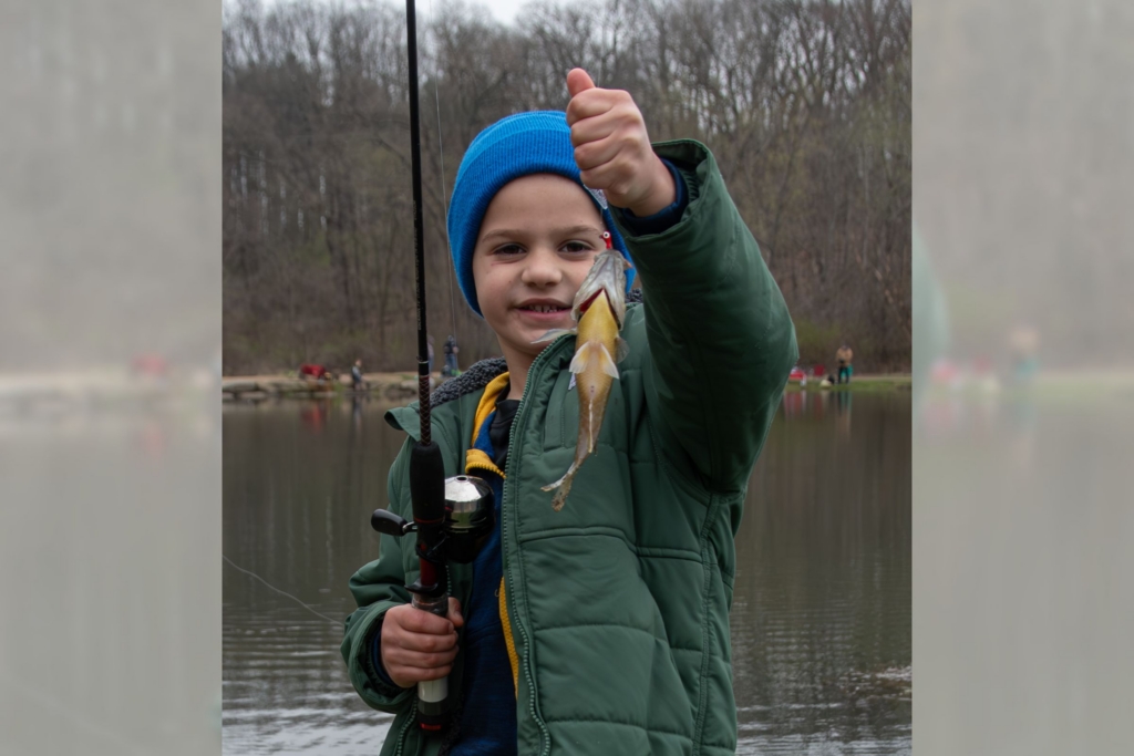 a young boy holds up the fish he caught at the annual Kids' Fishing Derby
