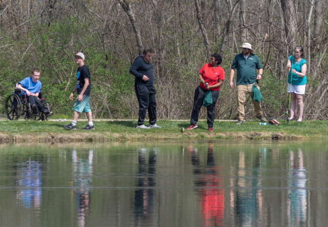 A group of people fishing along the edge of a pond.