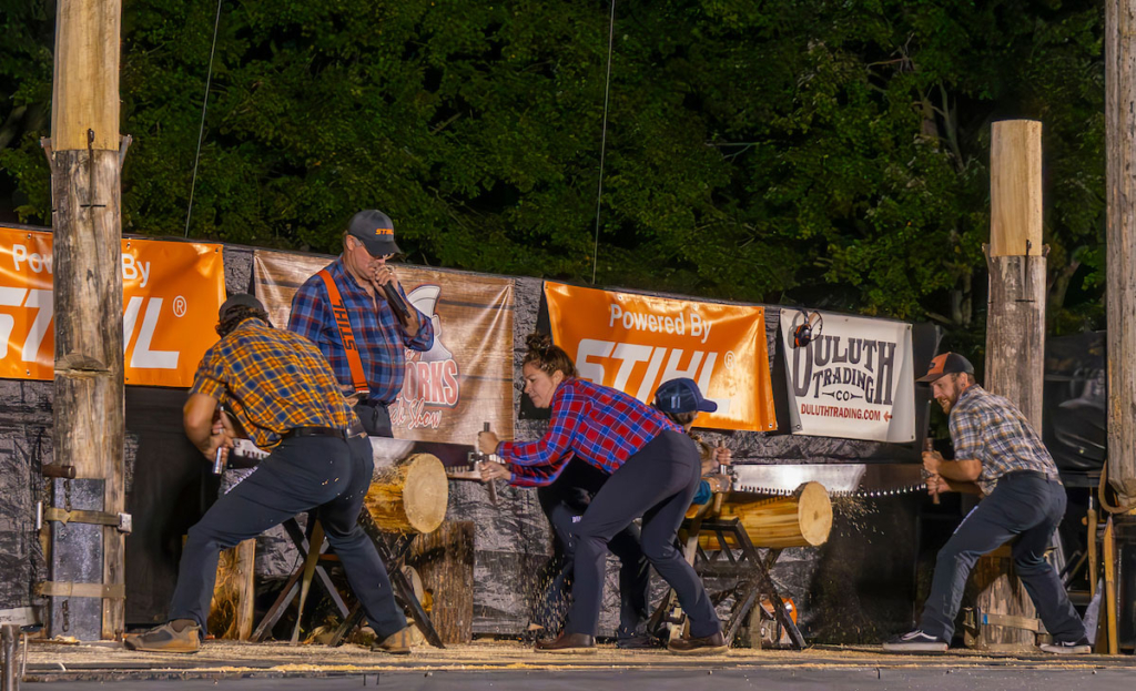 lumberjacks saw logs on a stage at nighttime