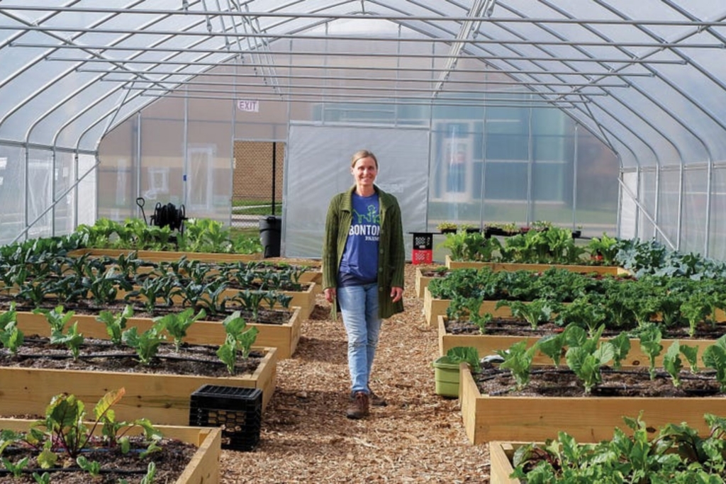 Lisa Nunn, director of Let's Grow Akron, walks through a greenhouse amongst rows of gardening beds.