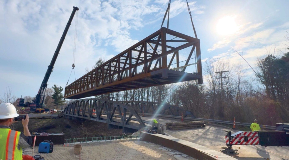 Cranes lift a metal pedestrian bridge placed as part of the Middlebury Road connector project