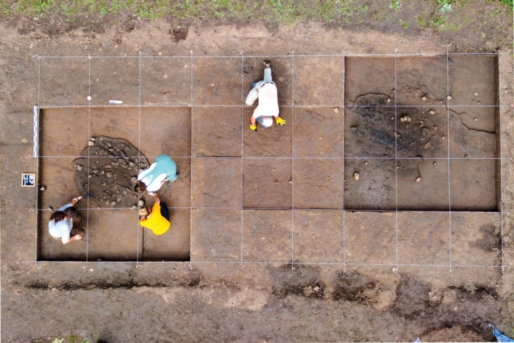 Three people work on excavating one of the earth ovens at the Everett Knoll Complex Site, while another person works in another area