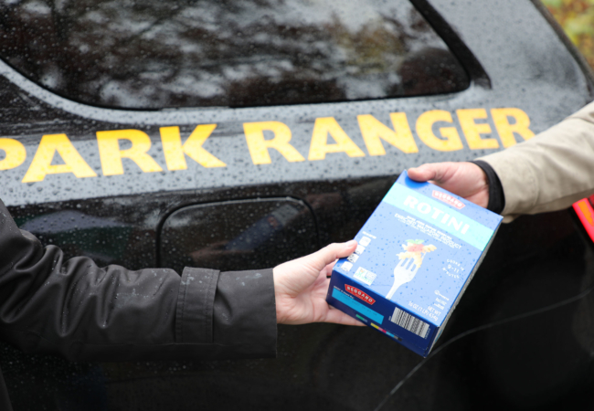 a blue box of pasta passes hands in front of a black vehicle with "park ranger" written on it in yellow