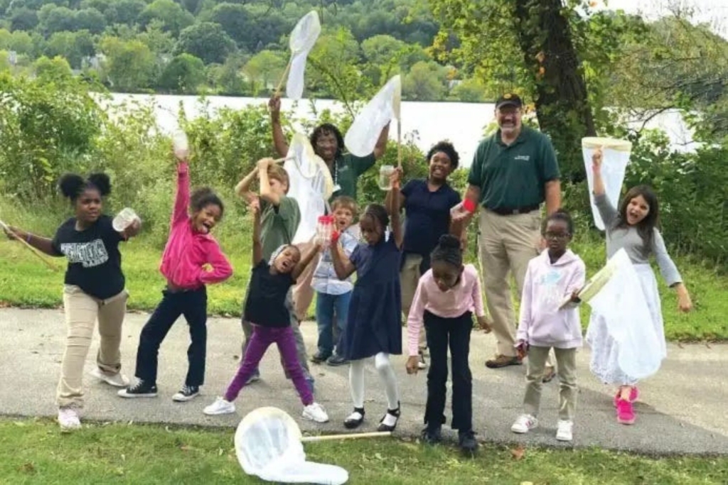 Two naturalists and ten Summit Lake Nature Club participants pose for a photo on a bug hunt along the Towpath Trail. Many of them hold butterfly nets and other items to catch and release bugs.
