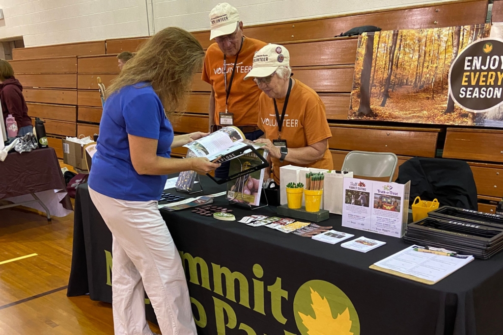 Ed and Judy interact with a visitor the Summit Metro Parks marketing table at a community event