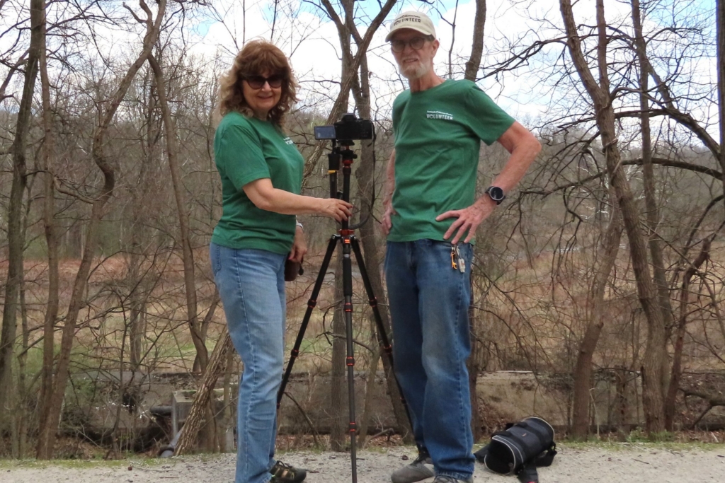 Volunteers Debbie and Alan stand on either side of a scope focused on an eagles' nest