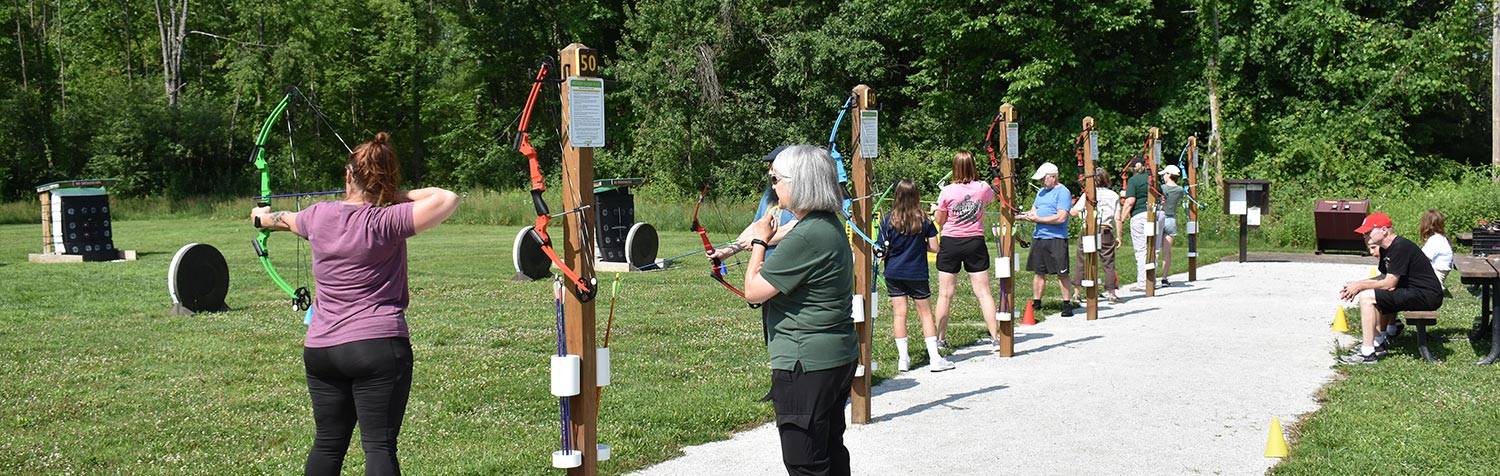 Archers lined up at an outdoor range, preparing to shoot arrows.