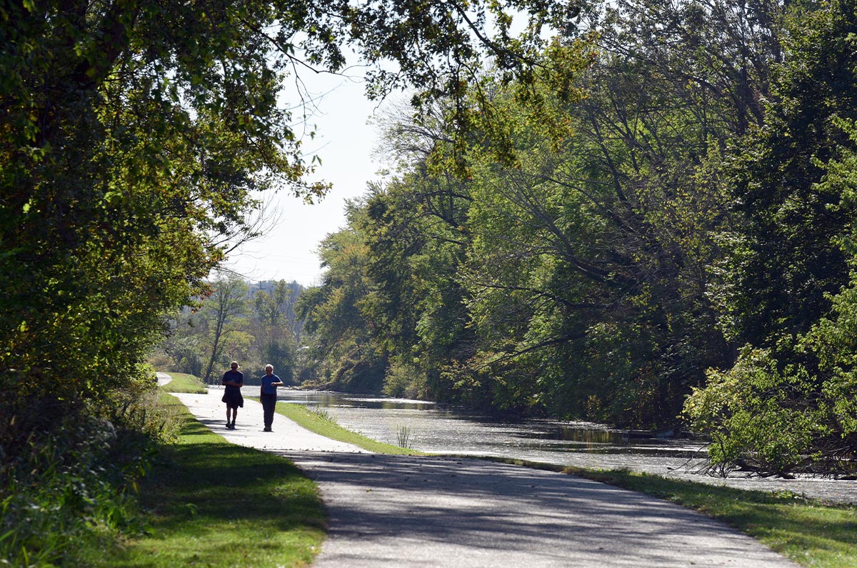 Two people walking along a limestone trail next to a canal.