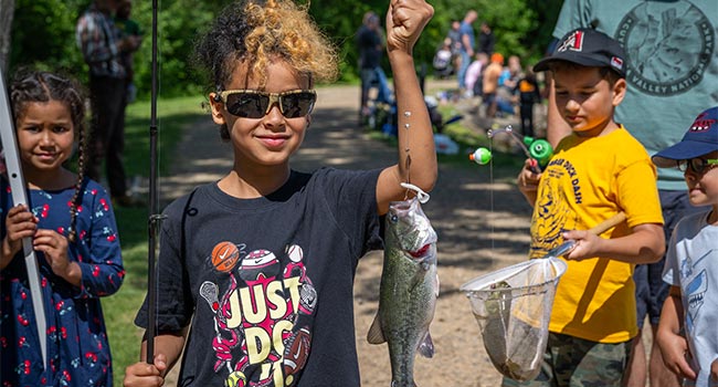 A child holds up a fish while smiling for the camera.