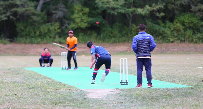 A pitcher throws a ball to a batter on a cricket pitch.