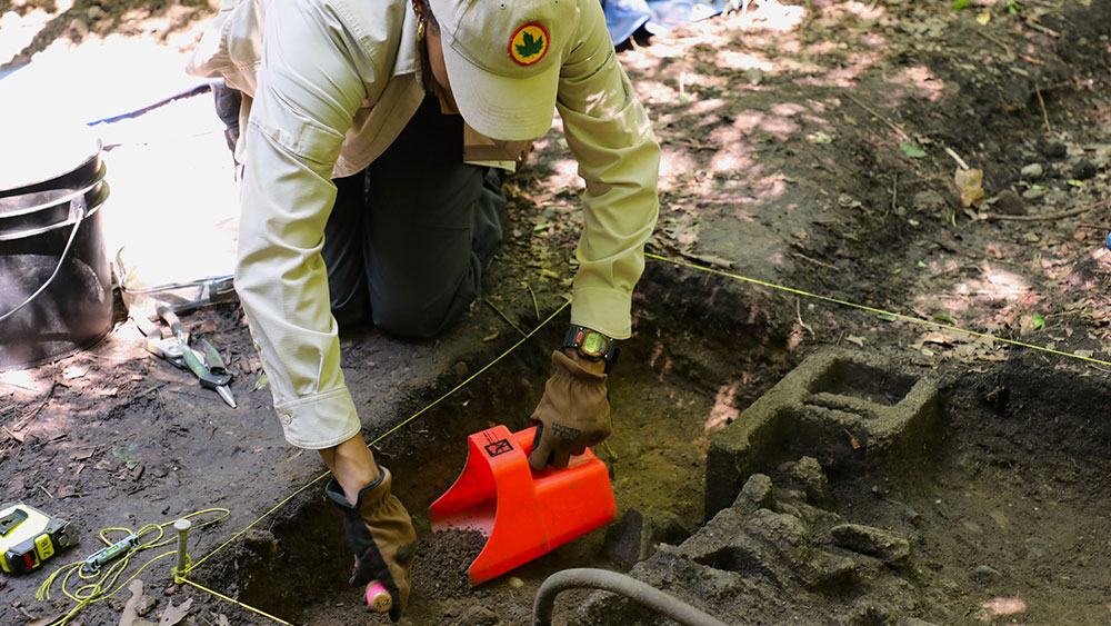 A person using various tools digs in the dirt