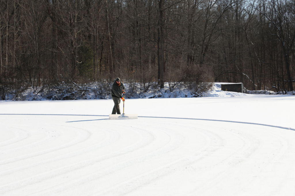 a man pushes snow toward the banks of Brushwood Lake