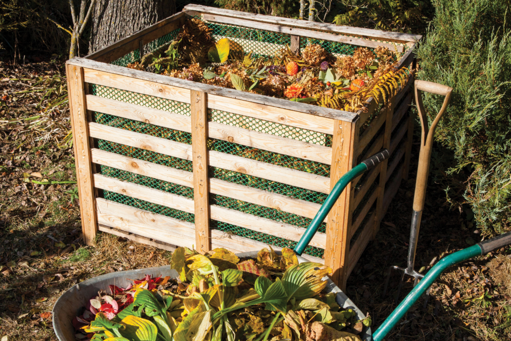 A wheelbarrow full of food scraps sits in front of a compost bin in a backyard