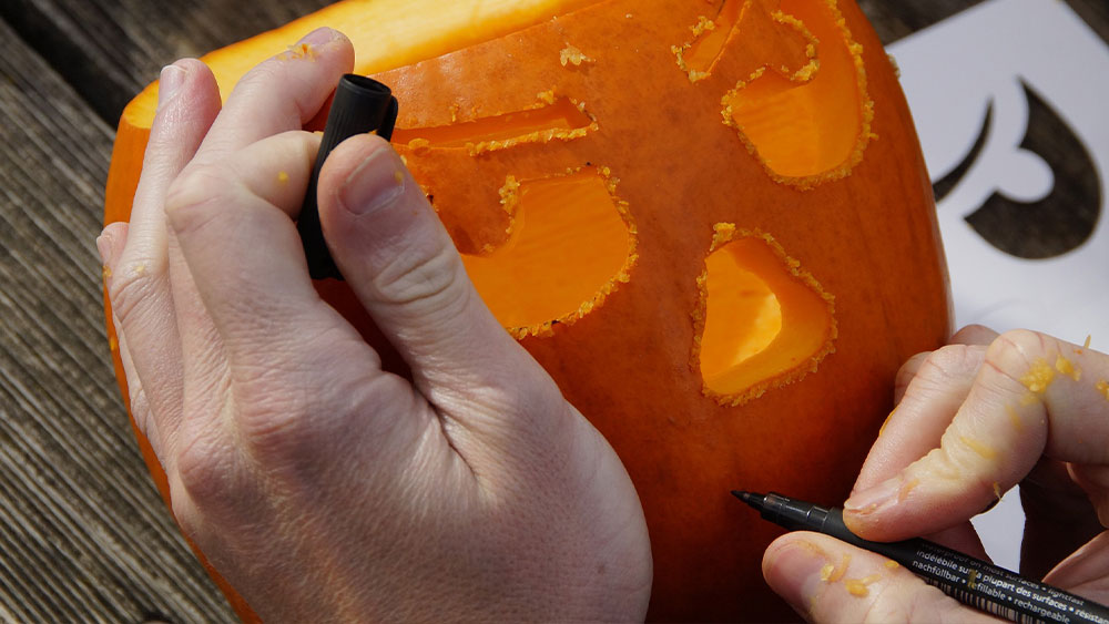 A person carving a face into a pumpkin.