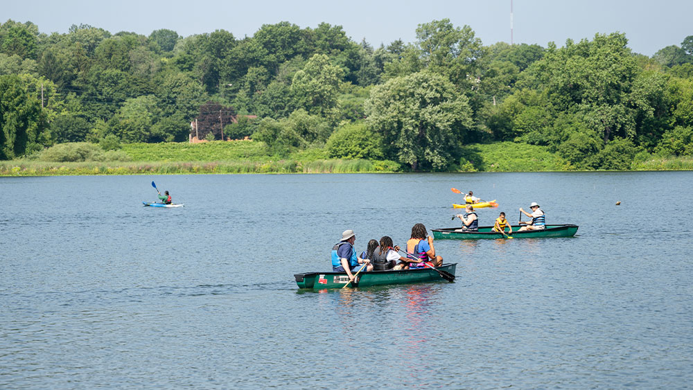 Several canoes and kayaks float across a large lake.