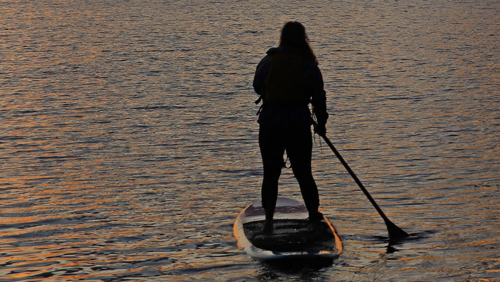 The silhouette of a paddleboarder on the water at sunset.
