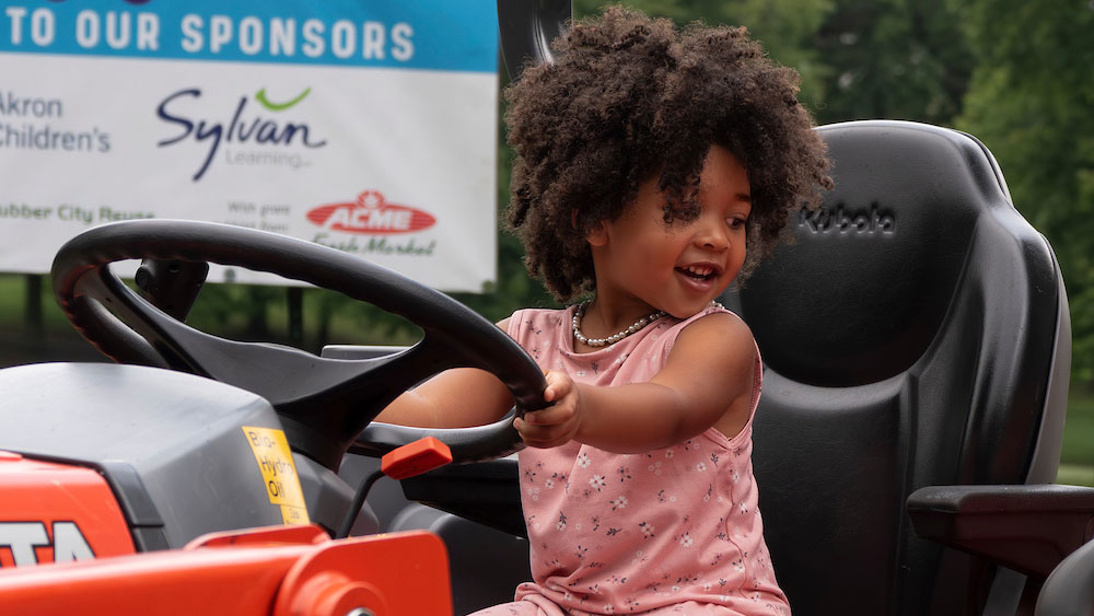 a child sits in a tractor seat with their hands on the wheel
