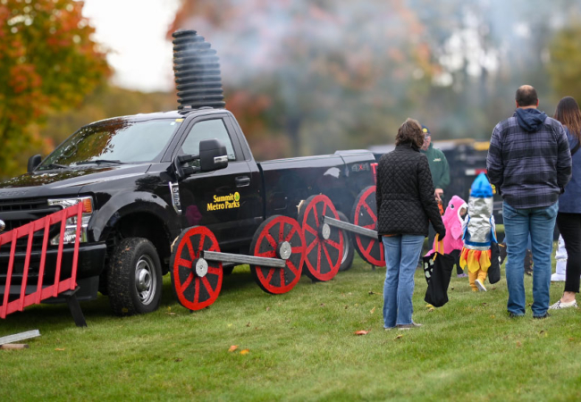 A pick-up truck with the SMP logo decorated as a train. Several people, including kids in costumes, are lined along the truck.