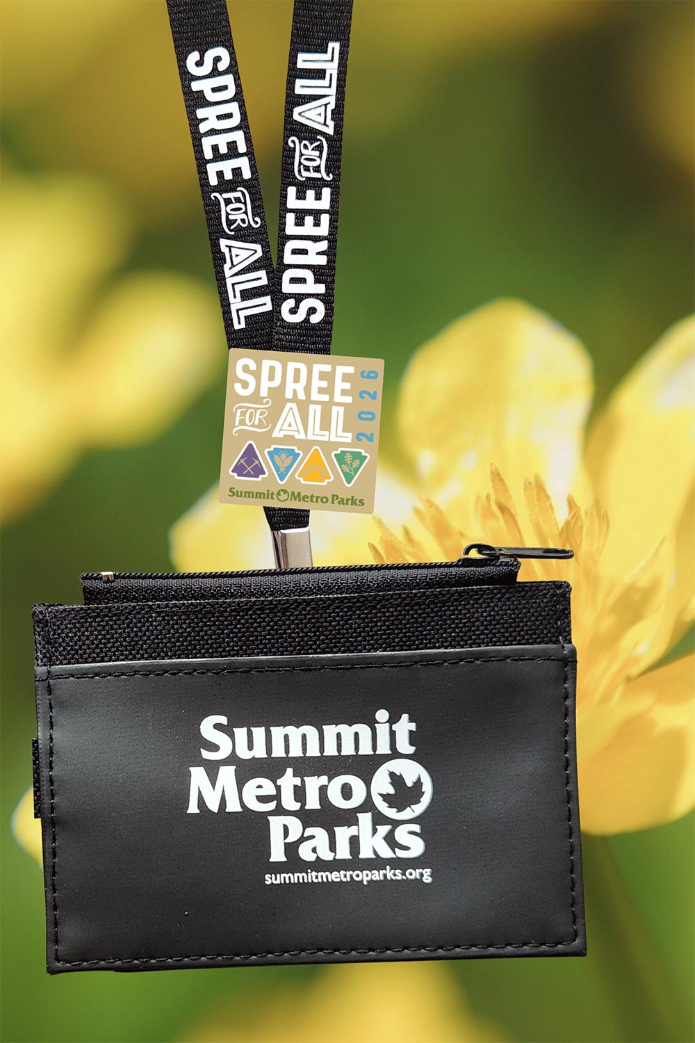 A black sipper pouch and lanyard overlayed on a photo of a yellow flower. The black pouch is labeled "Summit Metro Parks' and the lanyard is labeled Spree for All. A 2026 Spree for all pin is on the lanyard.