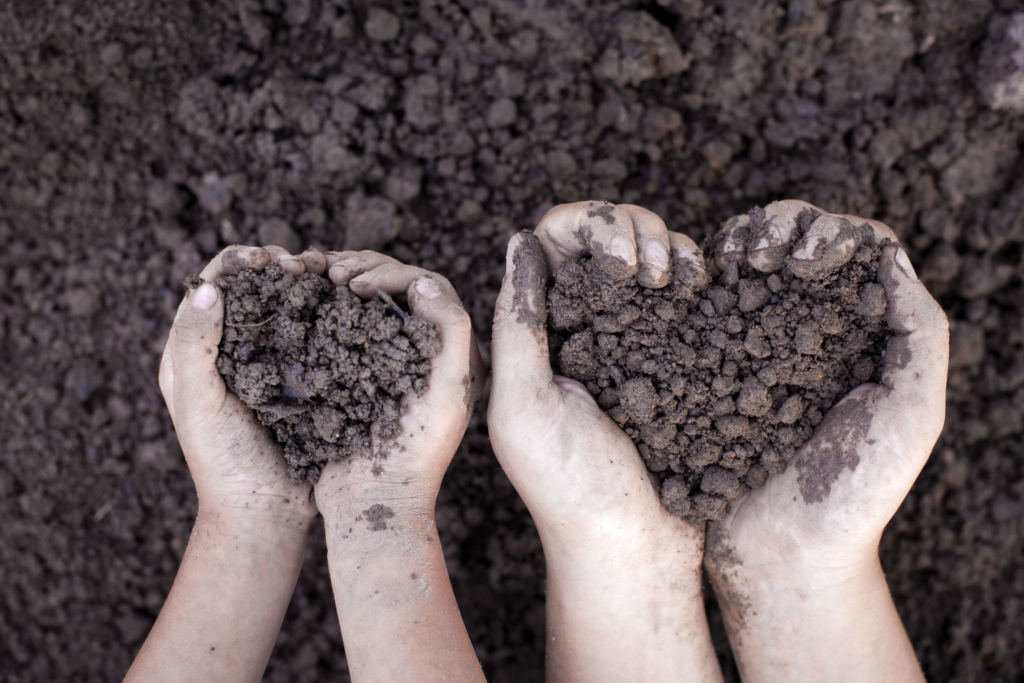 a child's hands and their parent's hands hold handfuls of soil that makes the shape of a heart