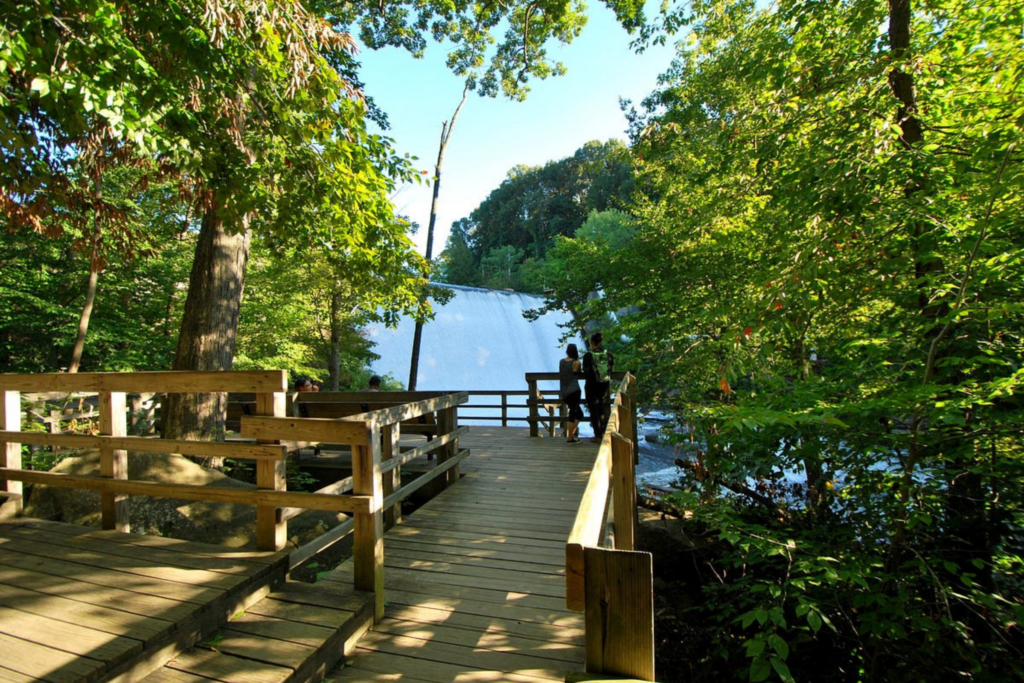 two people stand on the overlook at Gorge Metro Park, looking at the dam, while a few people sit behind them on benches