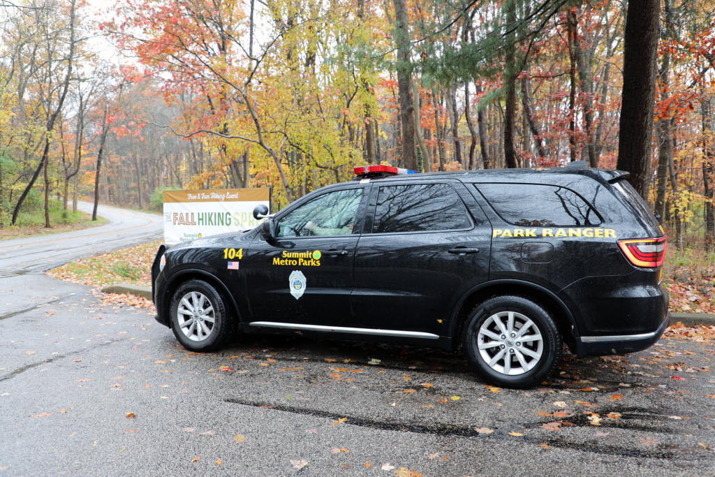 a black vehicle with sirens and yellow decals with fall foliage in the background
