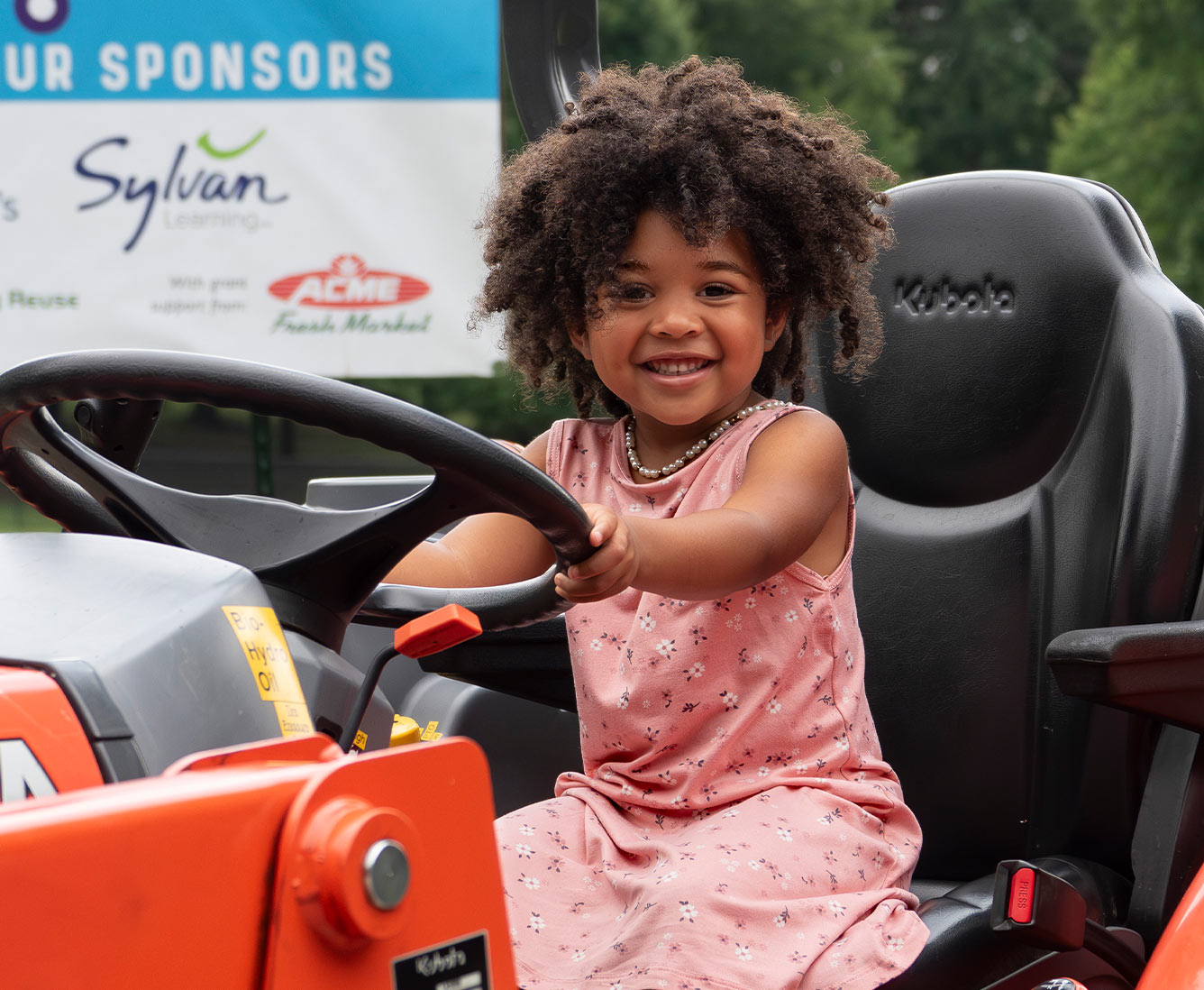 A young girl sits and smiles behind the wheel of a large tractor.