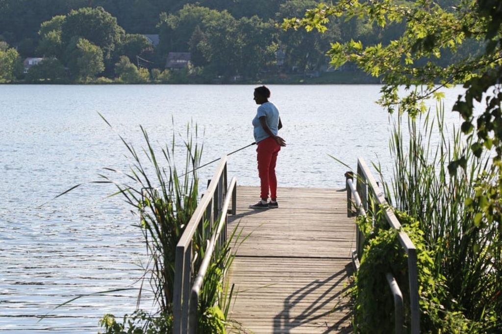 a Black woman stands at the end of a dock to fish on Summit Lake