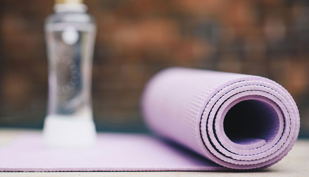 Close-up of a light purple yoga mat with water and a warm hued background.